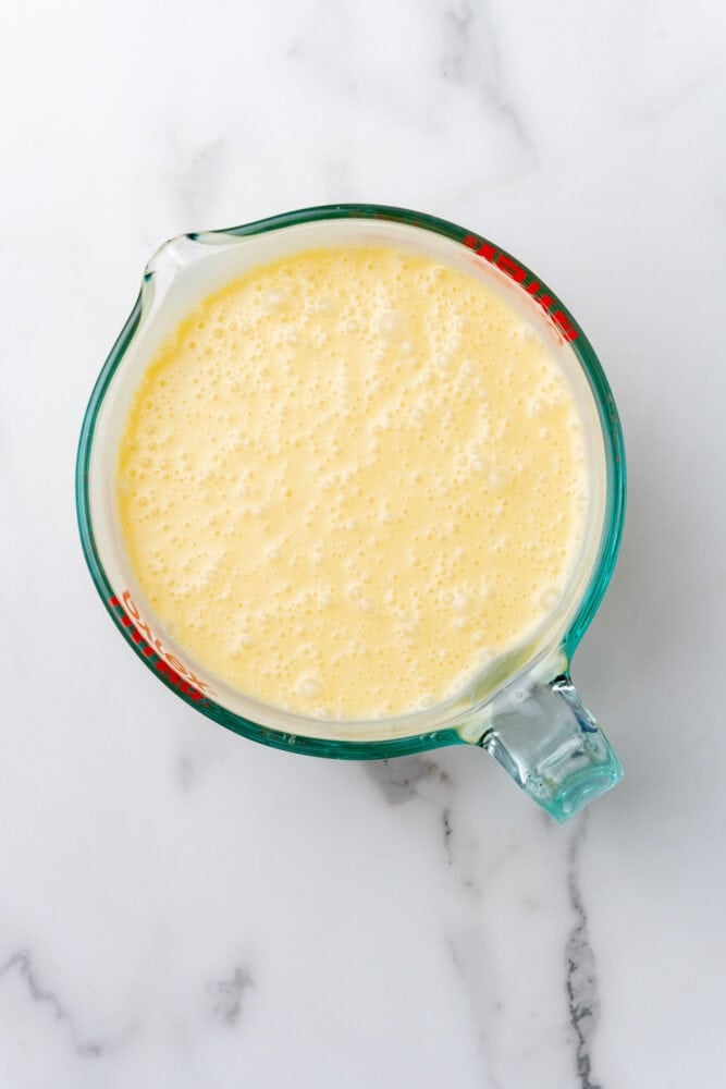Eggs, sweetened condensed milk, and coconut milk in a glass mixing bowl after blending.