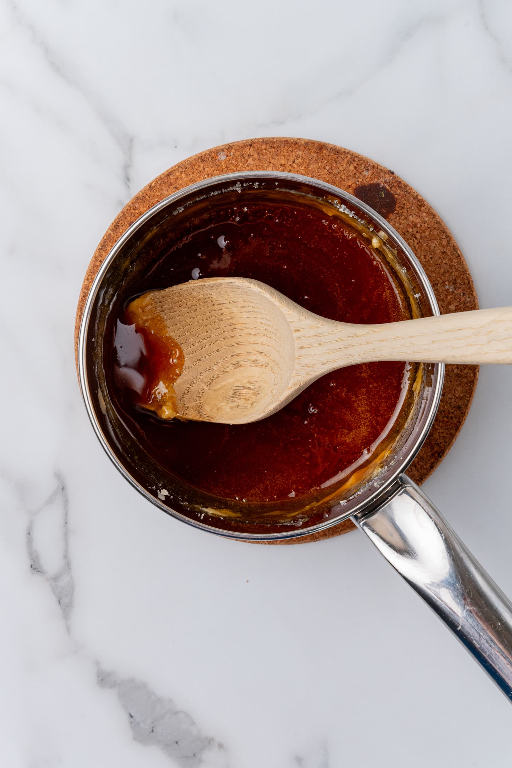 Caramelized sugar in a stainless steel sauce pan with a wooden spoon.