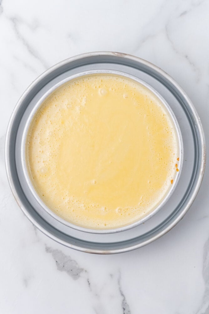 Eggs, sweetened condensed milk, and coconut milk blended together and poured into a cake pan. The cake pan is sitting inside a larger cake pan with water.