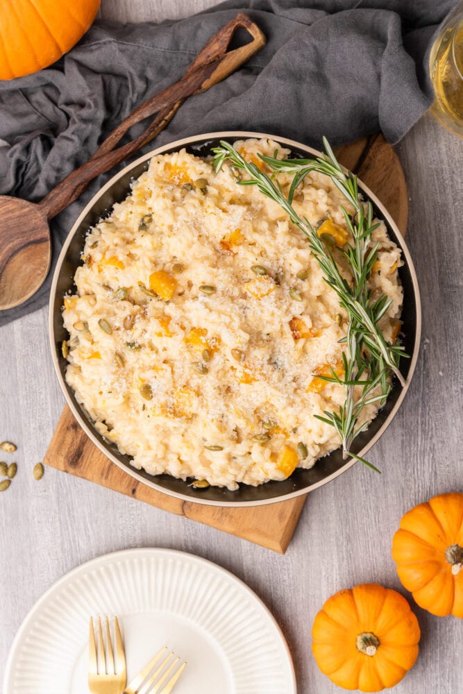 Overhead shot of pumpkin risotto in a serving bowl placed on a wood board and garnished with fresh rosemary.