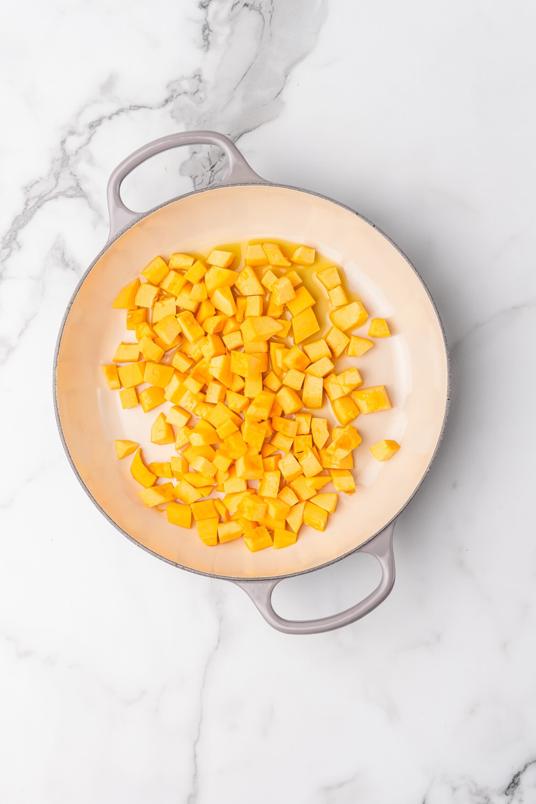 Raw diced pumpkin in an enameled cast iron pan.