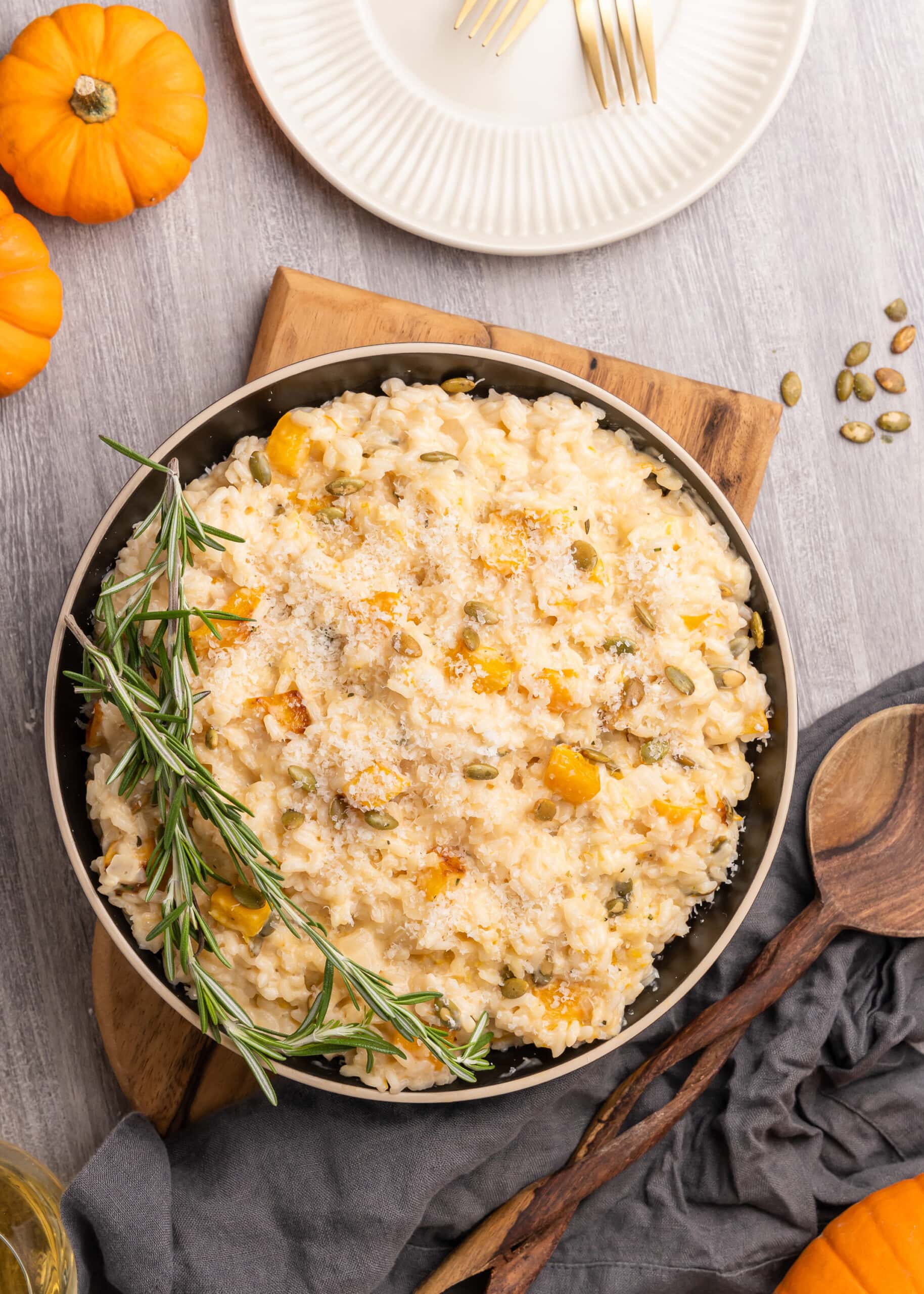 Overhead shot of serving bowl filled with pumpkin risotto on a wood board and garnished with fresh rosemary sprigs.