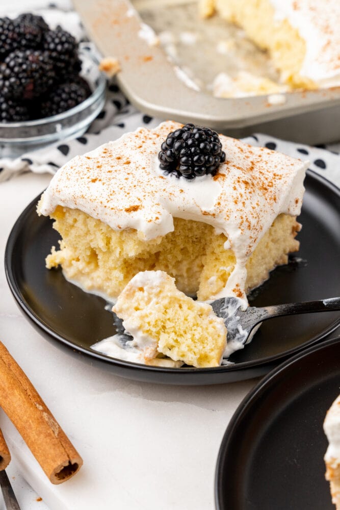 square slice of tres leches cake with blackberry on top and fork taking a bite