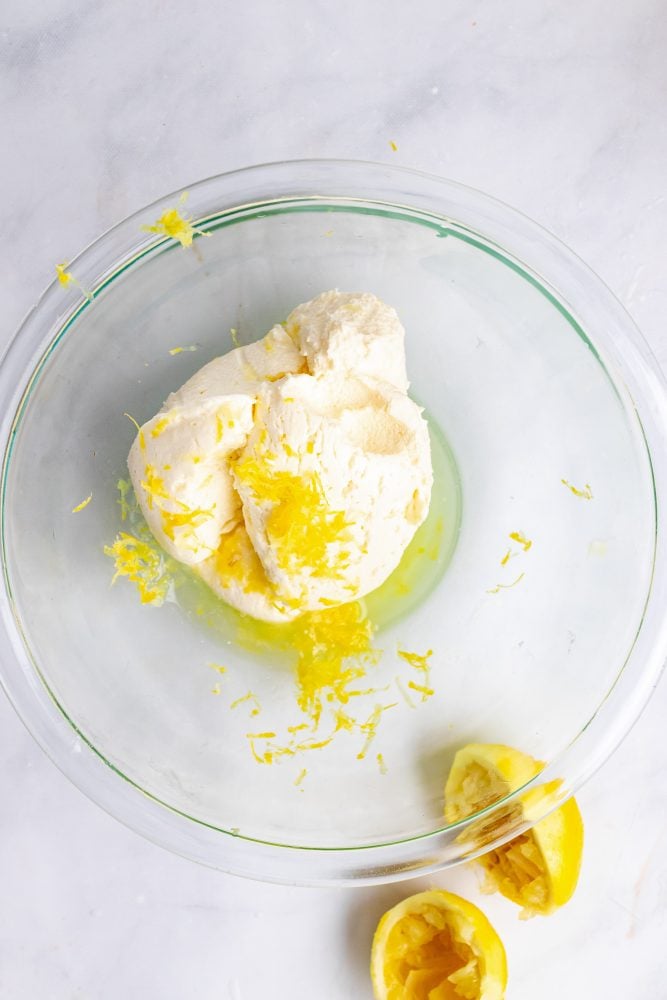 Overhead look at a clear glass bowl with mascarpone cheese, lemon zest and lemon juice.