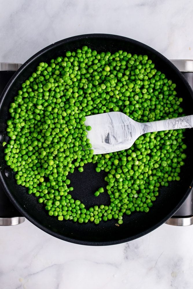 Overhead look at non-stick skillet full of peas and a spatula.