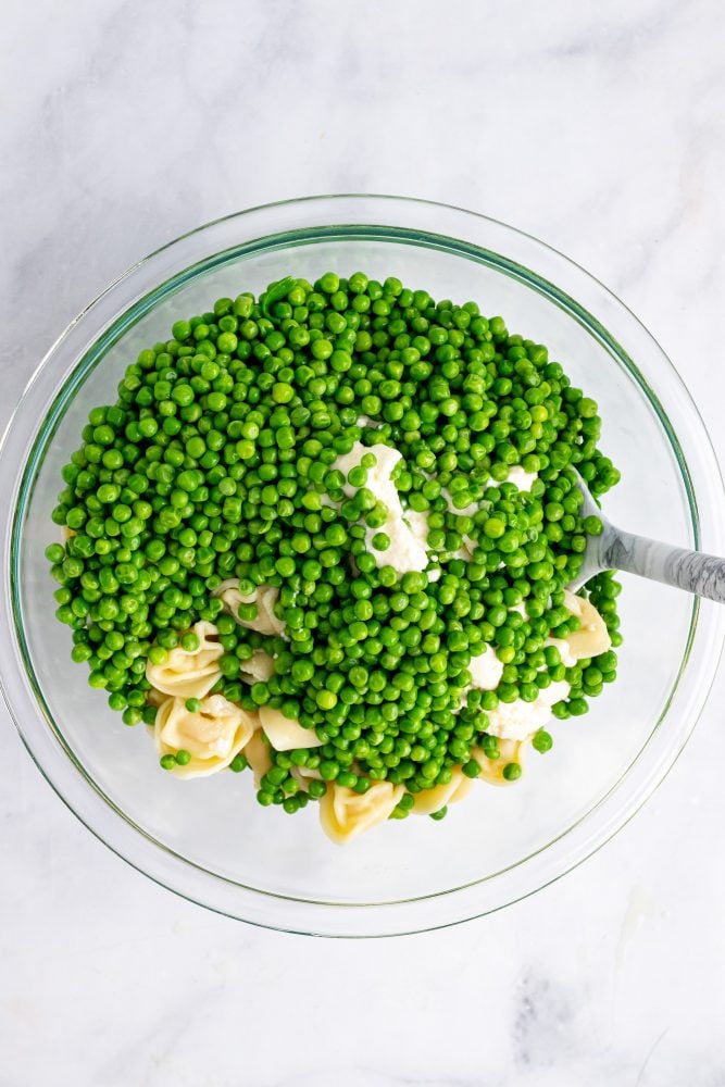 Clear glass bowl with peas, tortellini, and mascarpone cheese mixture.