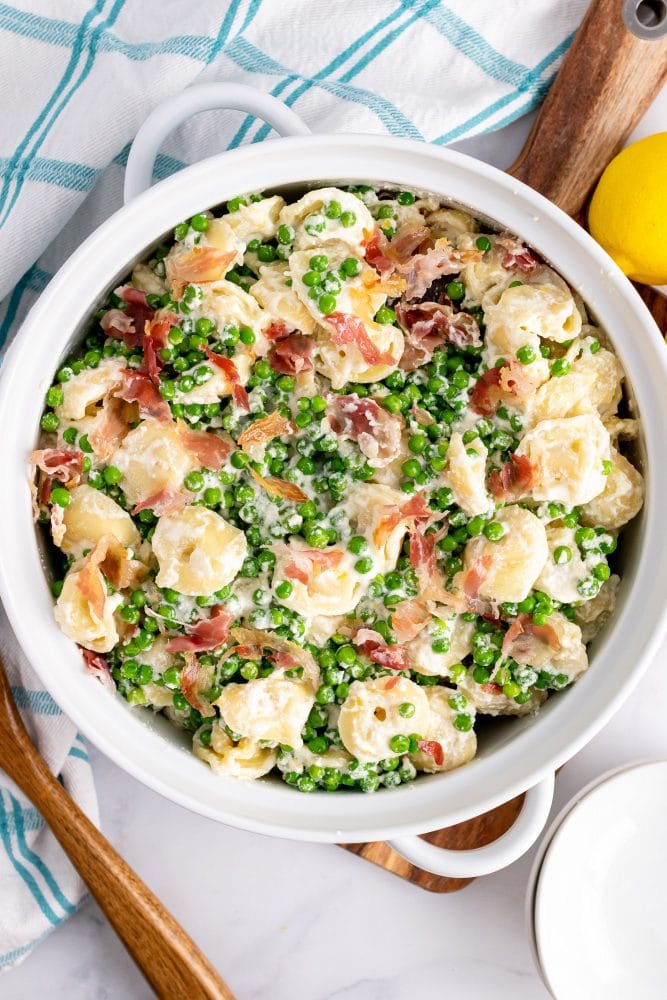 Overhead look at a white serving bowl with tortellini, peas, and pancetta.