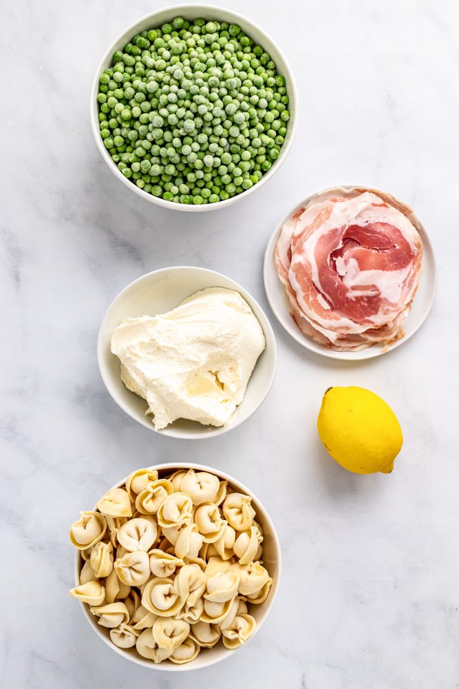 Overhead look at all 5 ingredients for this recipe: peas, pancetta, mascarpone cheese, one whole lemon, tortellini.