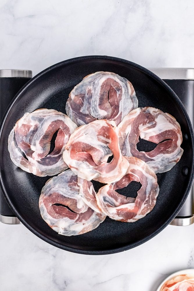 Overhead look at six slices of pancetta in a non-stick skillet.