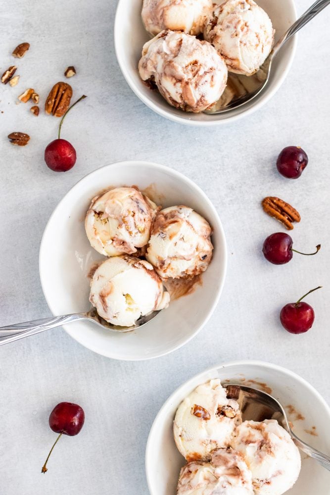 Overhead shot of three bowls of cherry ice cream with cherries and pecans sprinkled around them on the table.