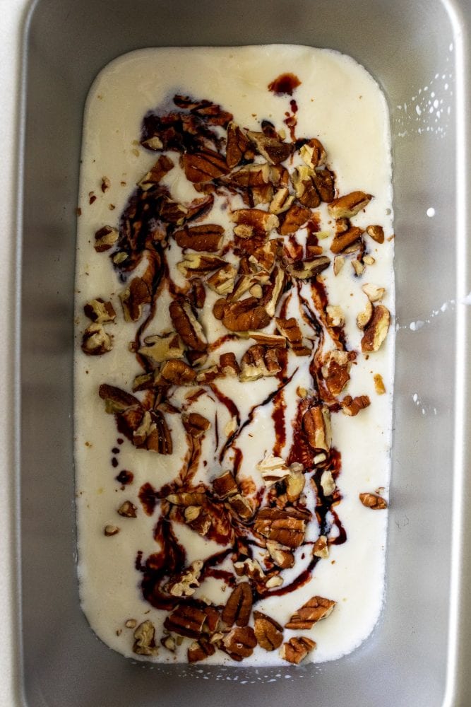 Overhead shot of plain ice cream base with cherry juice concentrate and pecans sprinkled on top.