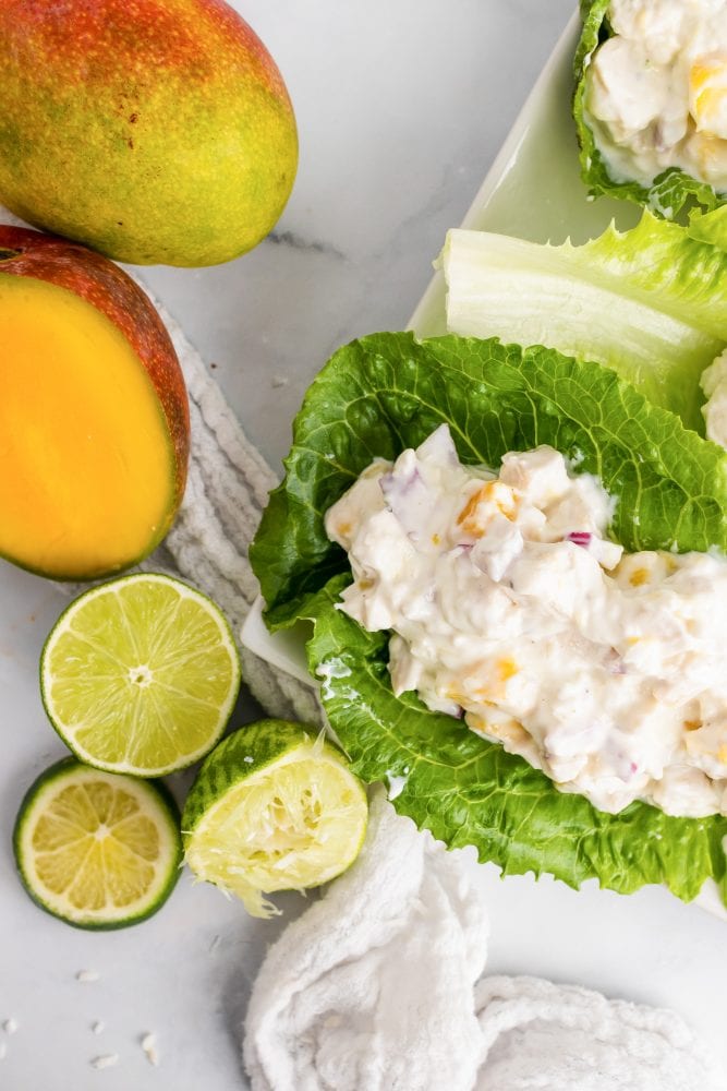 Overhead look at romaine lettuce filled with mango chicken salad and sliced mangos and limes on the side.