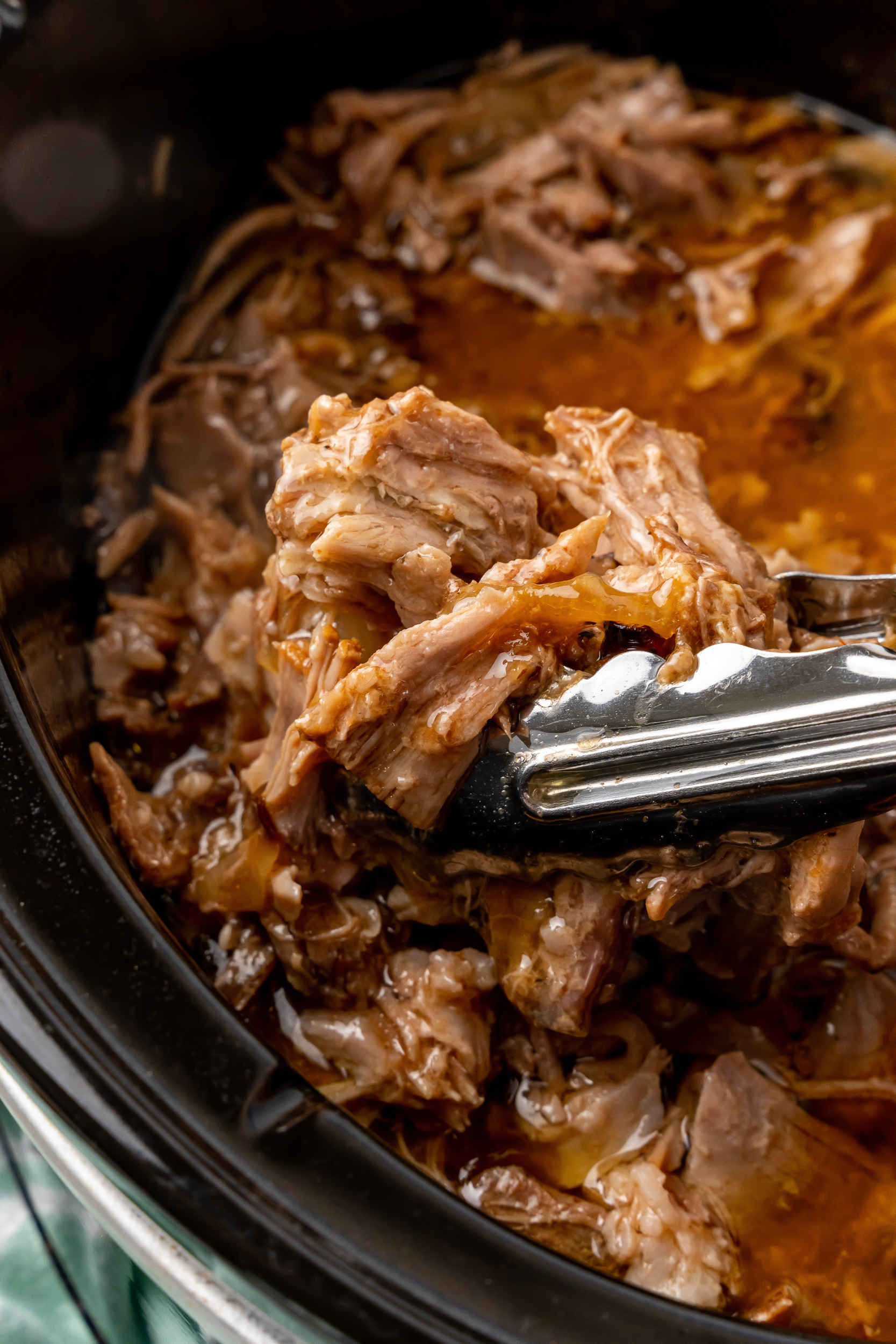 close up of pulled pork in crock pot beging served with tongs