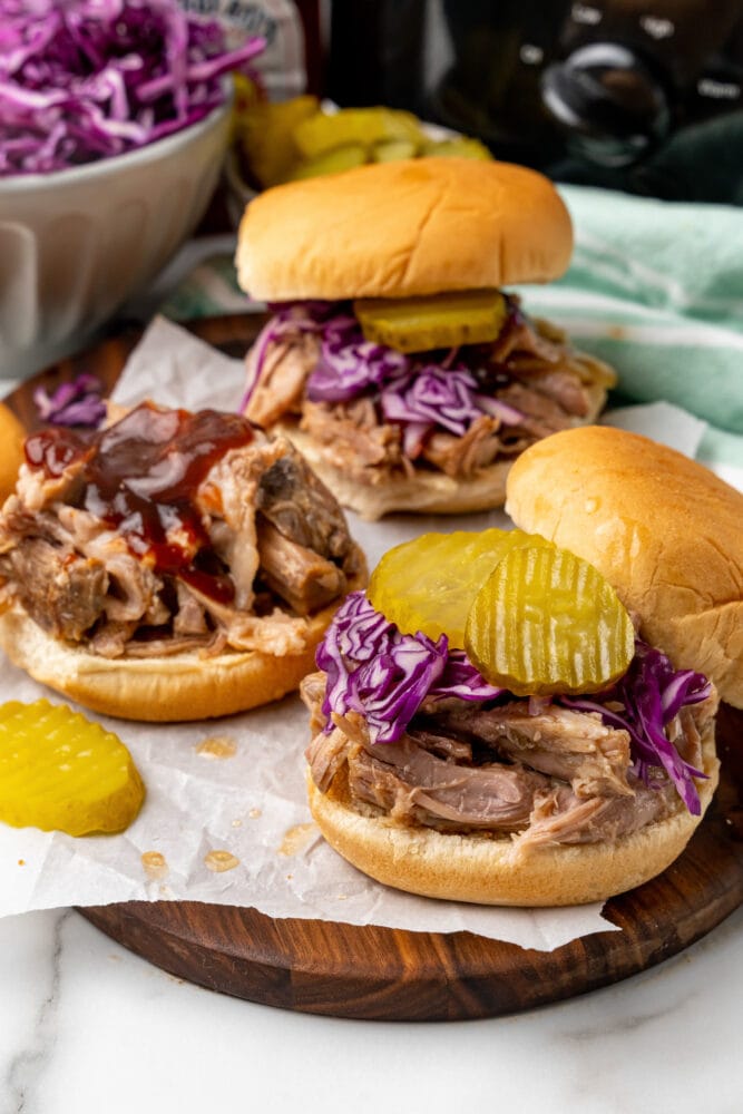 pulled pork sandwiches with pickles, bbq sauce, red cabbage slaw, and crock pot in the background