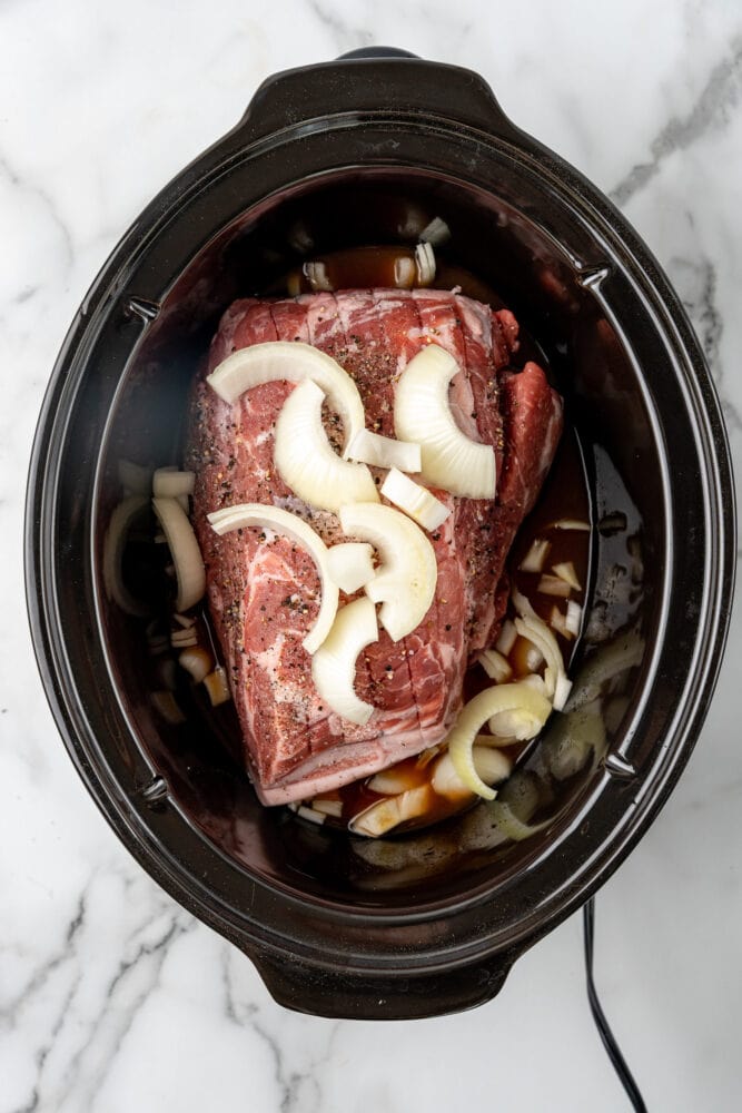seasoned pork shoulder and onions inside crock pot with cider and bbq sauce