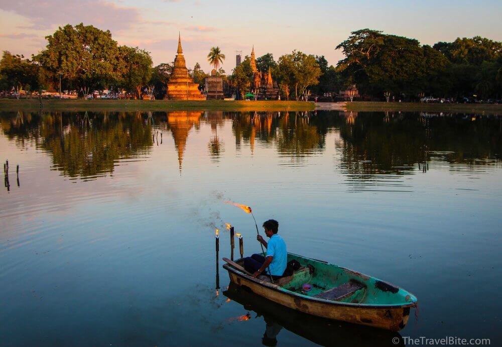 Boat lighting torches in the water outside of a temple in Thailand