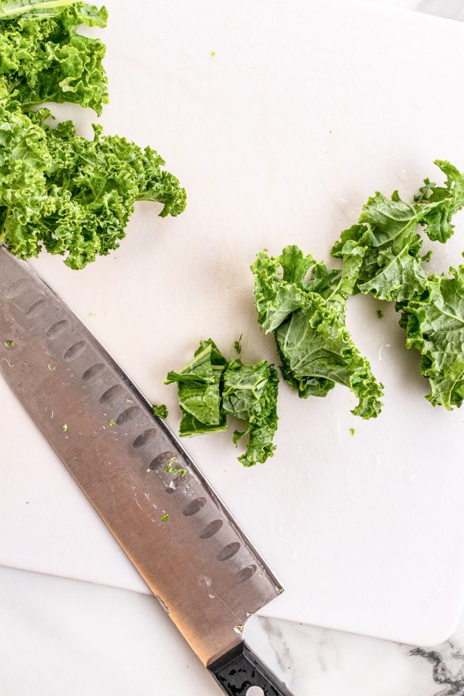 Chef's knife and chopped kale on cutting board.