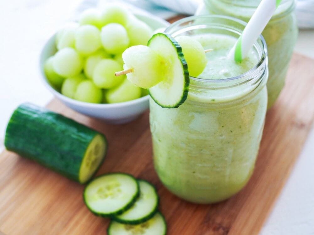 Cucumber Melon Smoothie on top of a cutting board with a bowl of melon and sliced cucumber.