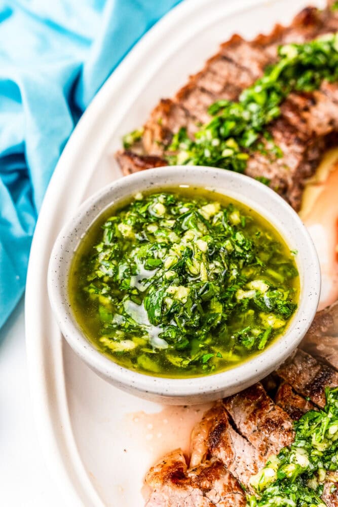 Close up of a small bowl of chimichurri sauce. You can see the diced herbs, garlic, and oil.