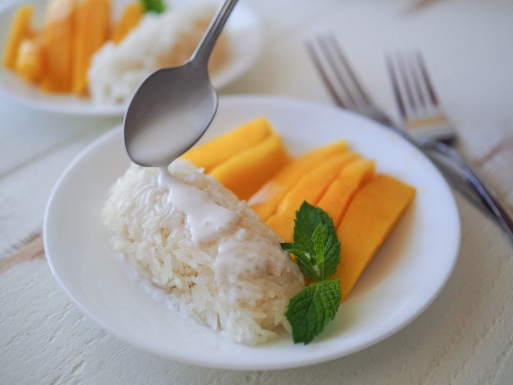 Adding more coconut milk to sticky rice with a spoon. 