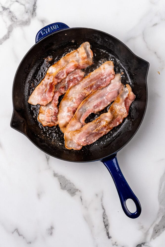 bacon frying in a blue staub skillet