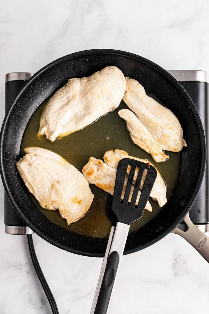 Adding apple cider to frying pan with browned chicken breasts