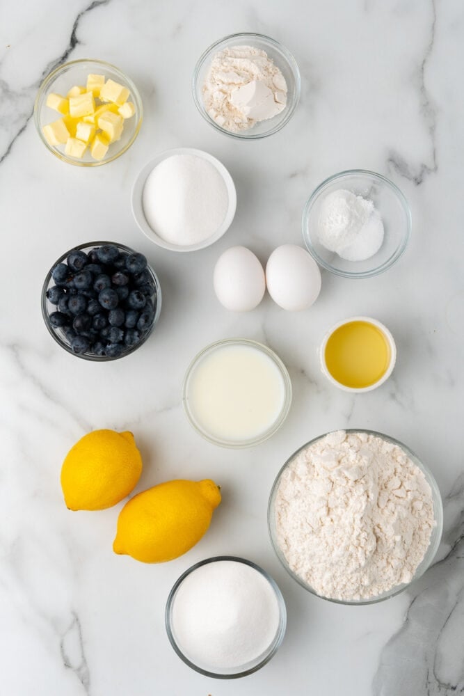 Ingredients for lemon blueberry muffins including all-purpose flour, white sugar, salt, baking powder, vegetable oil, eggs, lemons, milk, blueberries, butter