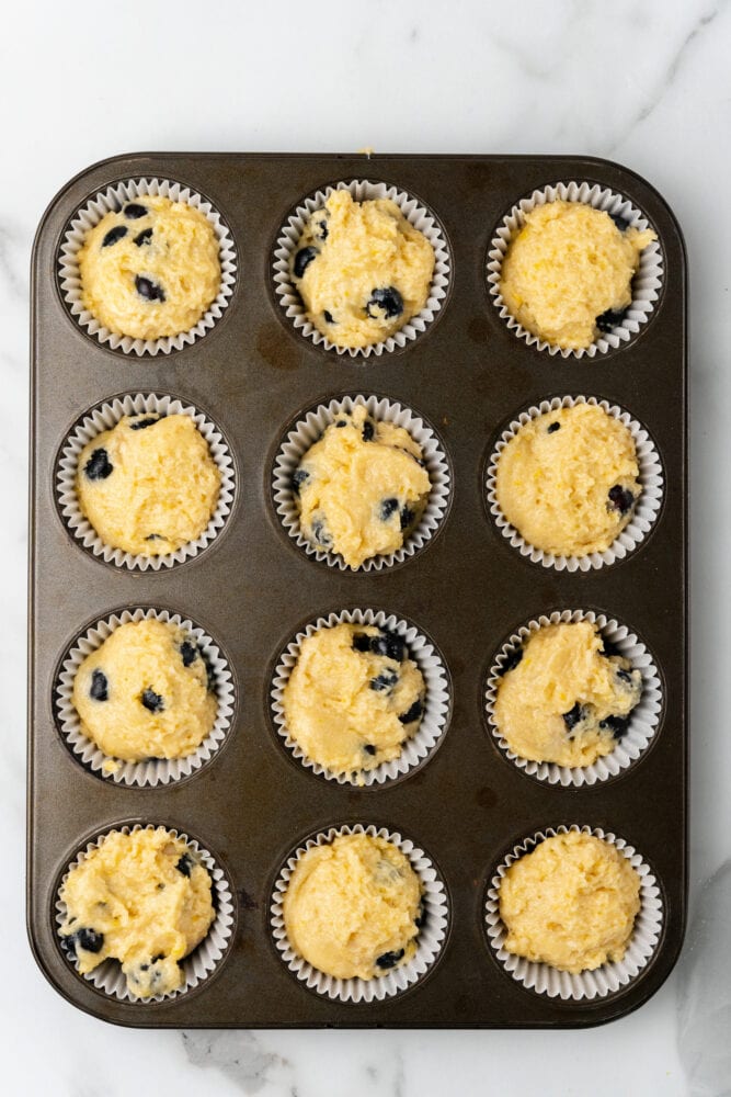 lemon blueberry muffin batter in paper cups in a muffin tin ready to be baked
