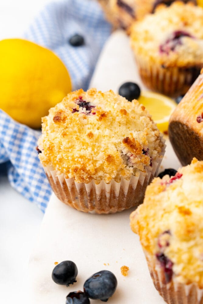 closeup of lemon blueberry muffin with fresh lemons and blueberries on the white board around it