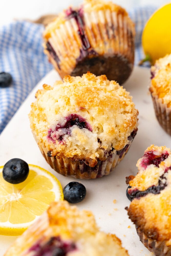 fresh baked lemon blueberry muffin on white serving board with blue and white checkered cloth in background