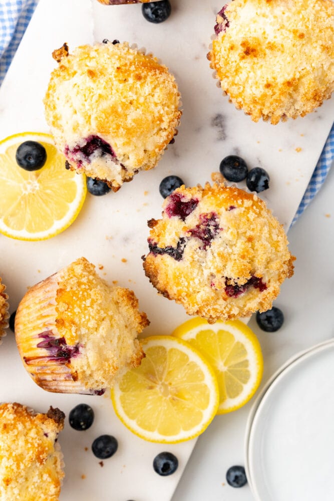 Overhead view of lemon blueberry muffins on white cutting board with lemon slices and bluberries surrounding muffins.