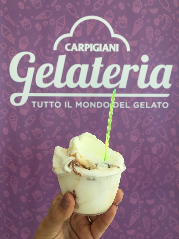 A little cup of gelato in front of a purple sign for Carpigiani Gelateria.
