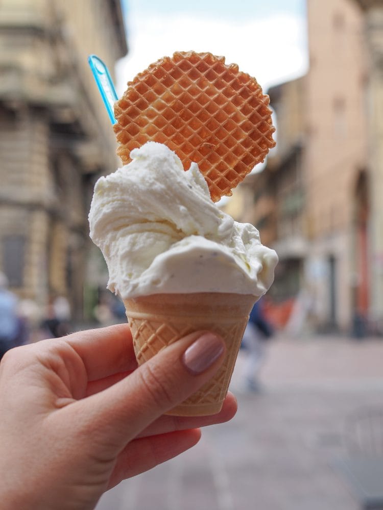 A creamy vanilla gelato with a large waffle cookie held up in the historic part of Bologna.