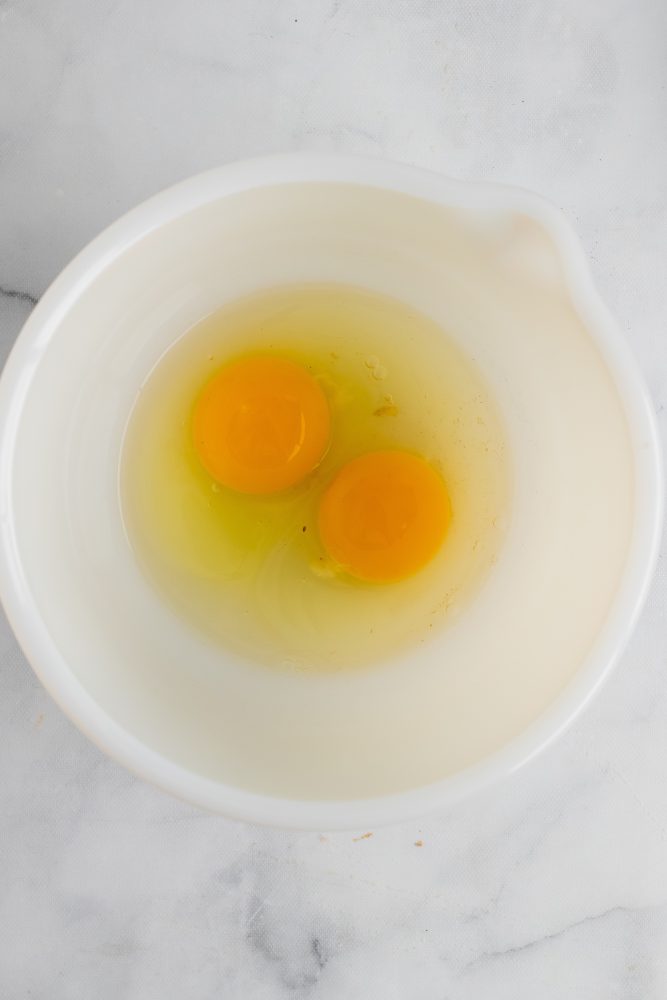 Two eggs in a bowl before getting whisked together.