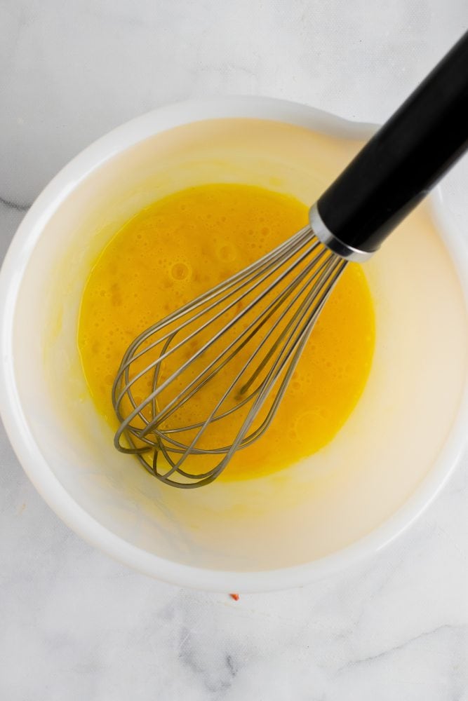 Whisked eggs in bowl with whisk resting on the side.