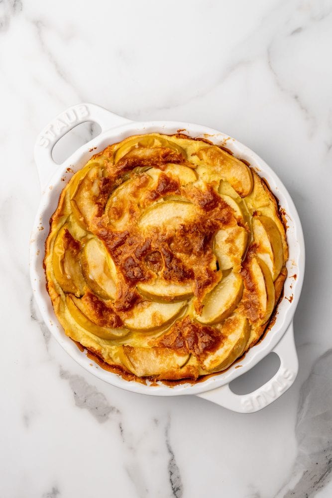 Overhead photo of baked German apple pancake in a white staub enameled cast iron pie pan.