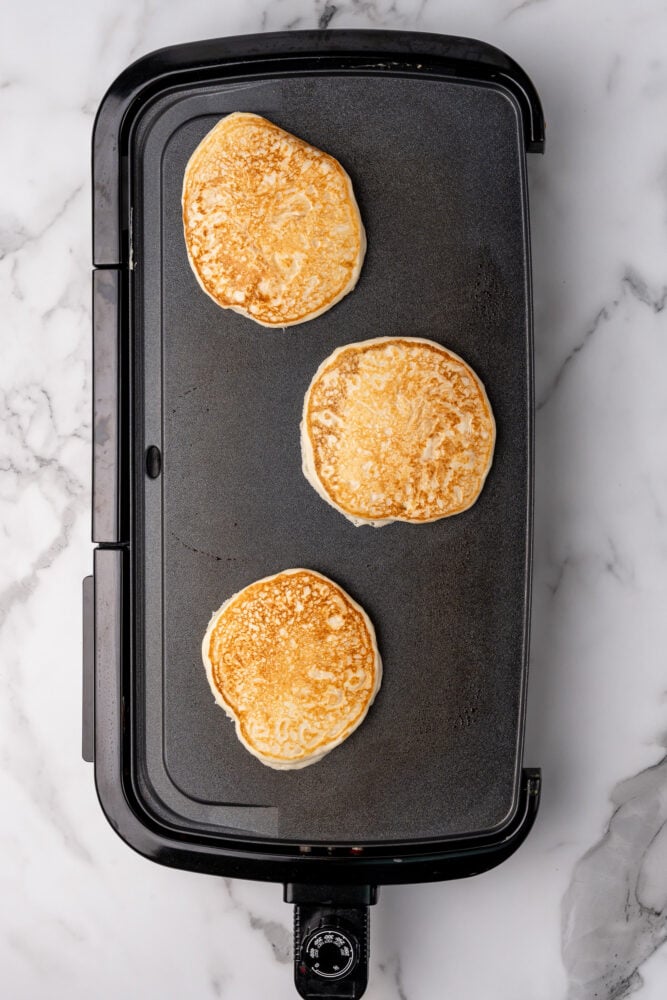 Three golden brown and fluffy pancakes on a griddle.