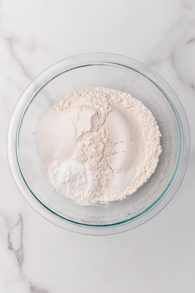 Dry ingredients to make homemade pancakes in a clear glass bowl including flour, sugar, baking powder, and salt.