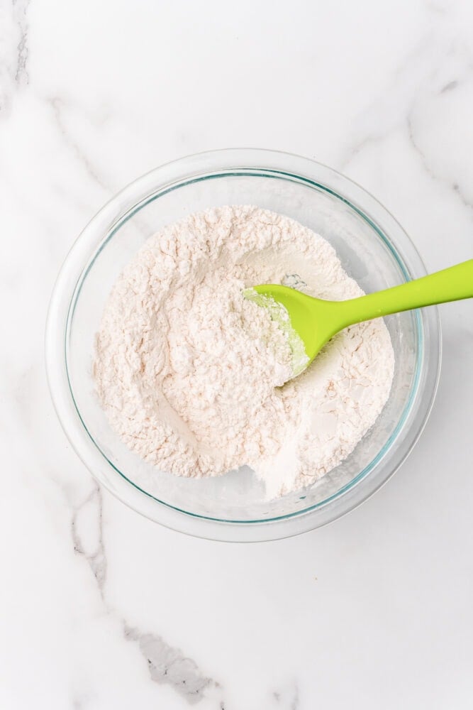 Dry ingredients to make homemade pancakes in a clear glass bowl, mixed together with a lime green spoon.