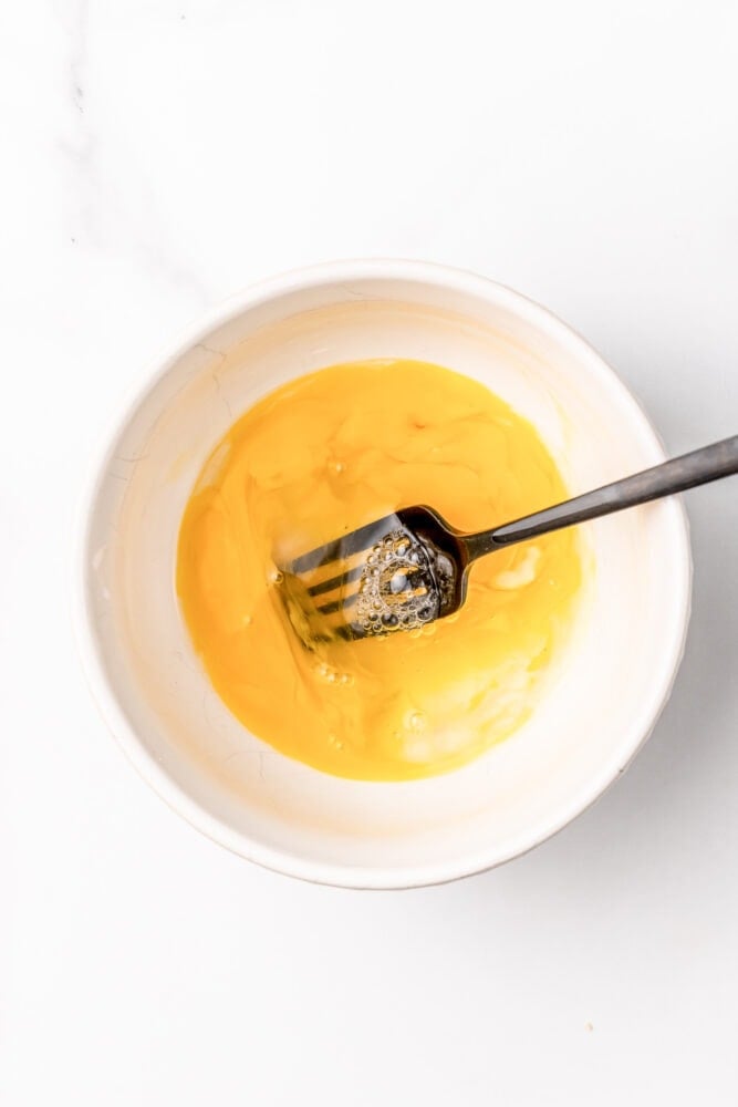 Small white bowl with egg whisked with a fork.