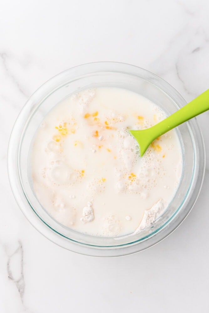 Milk and egg added to dry ingredient pancake mixture with a lime green spoon ready to mix together.