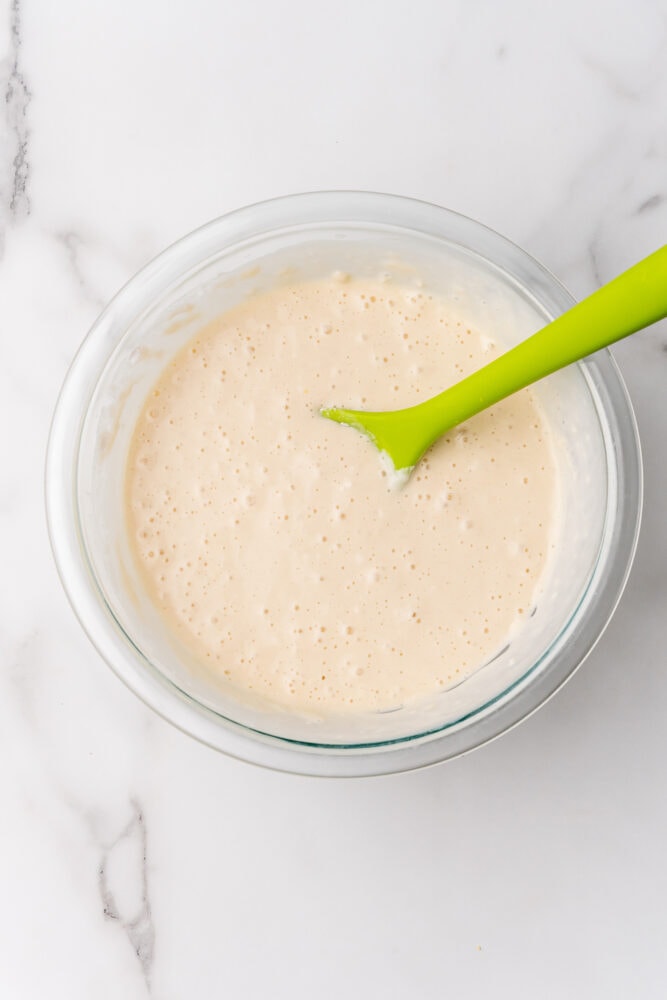 Pancake batter mixed together in a clear glass bowl with a lime green spoon.