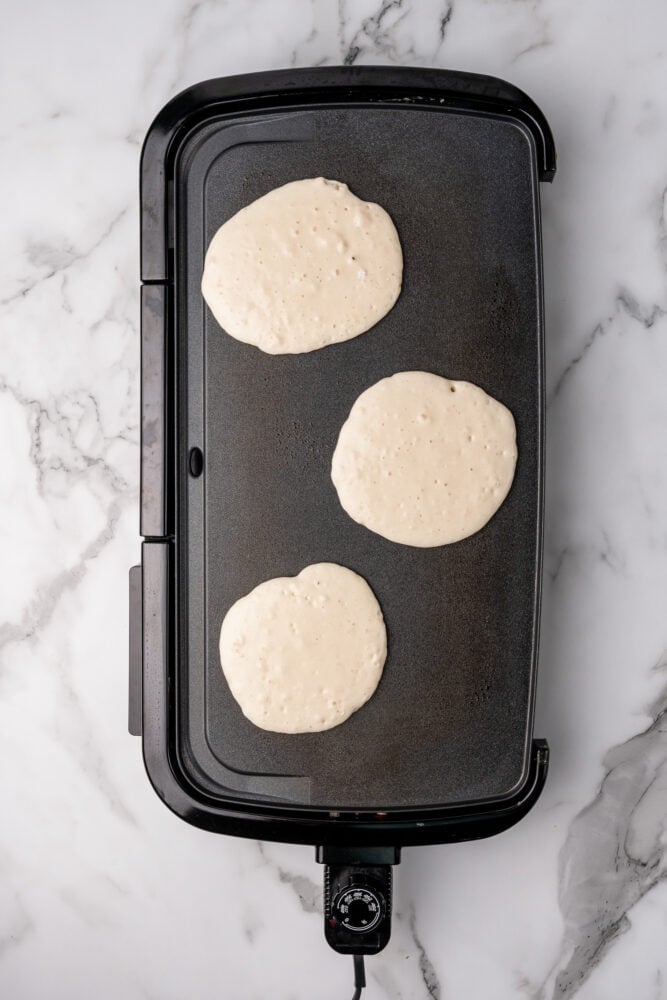 Uncooked pancake batter poured to make three small pancakes on a griddle.
