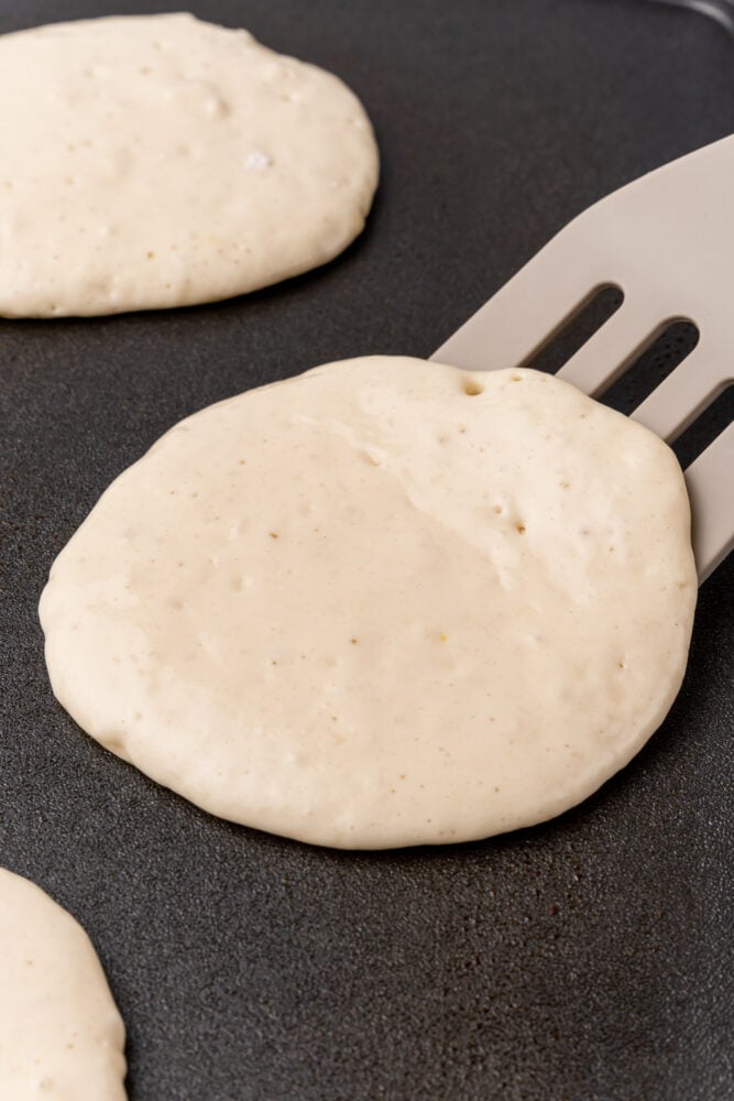 Closeup of spatula flipping a pancake that has bubbles formed on top.