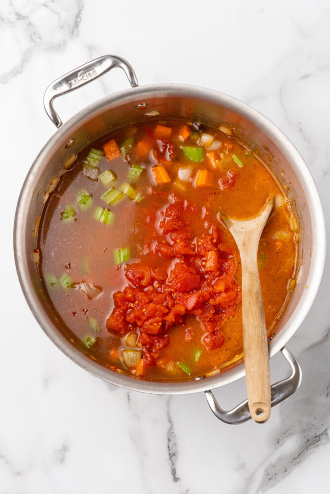 Adding canned tomatoes to soup pot with broth and vegetables.