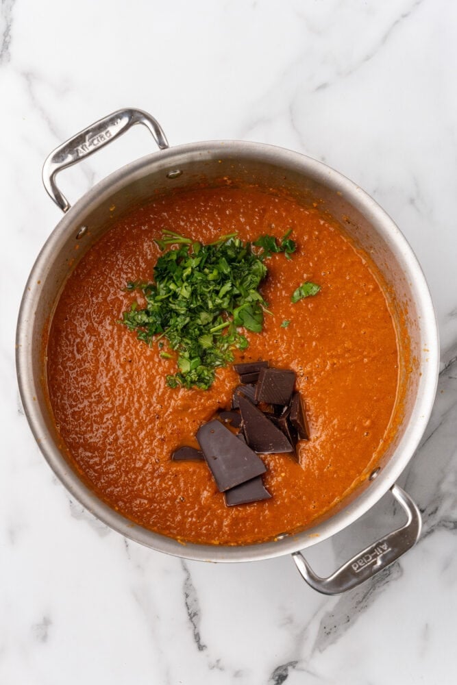 Adding chocolate and fresh parsley to soup pot filled with spicy tomato soup.
