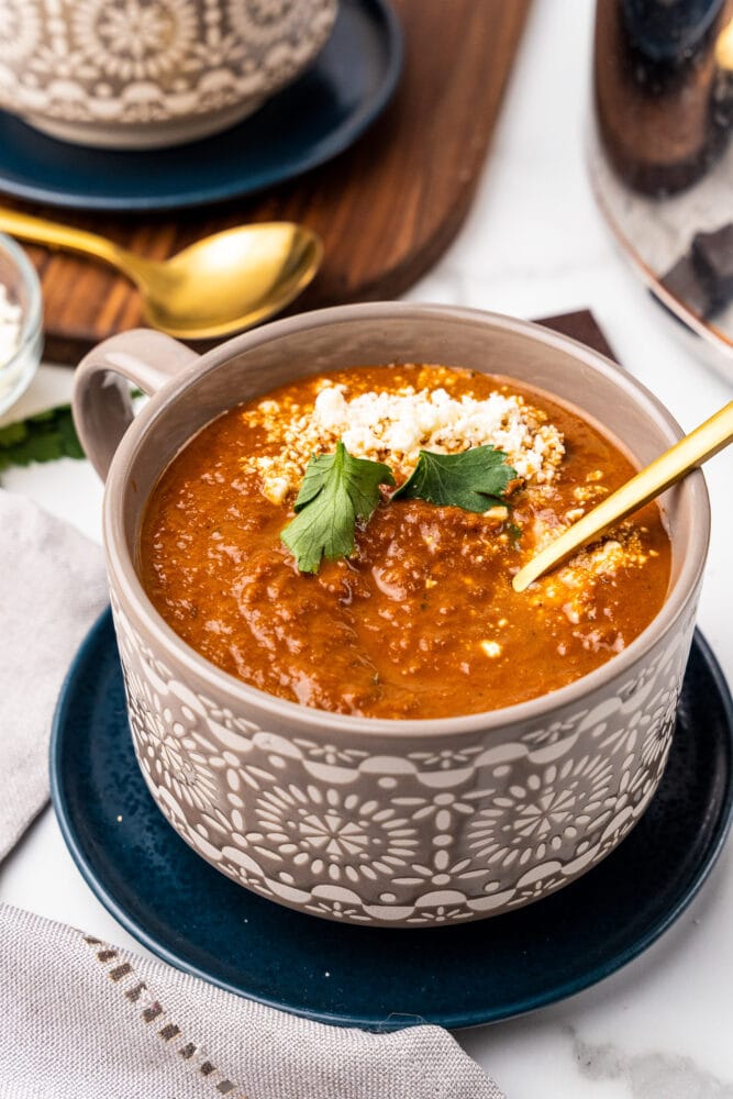 bowl of spicy tomato soup in a grey bowl, garnished with cheese and parsley