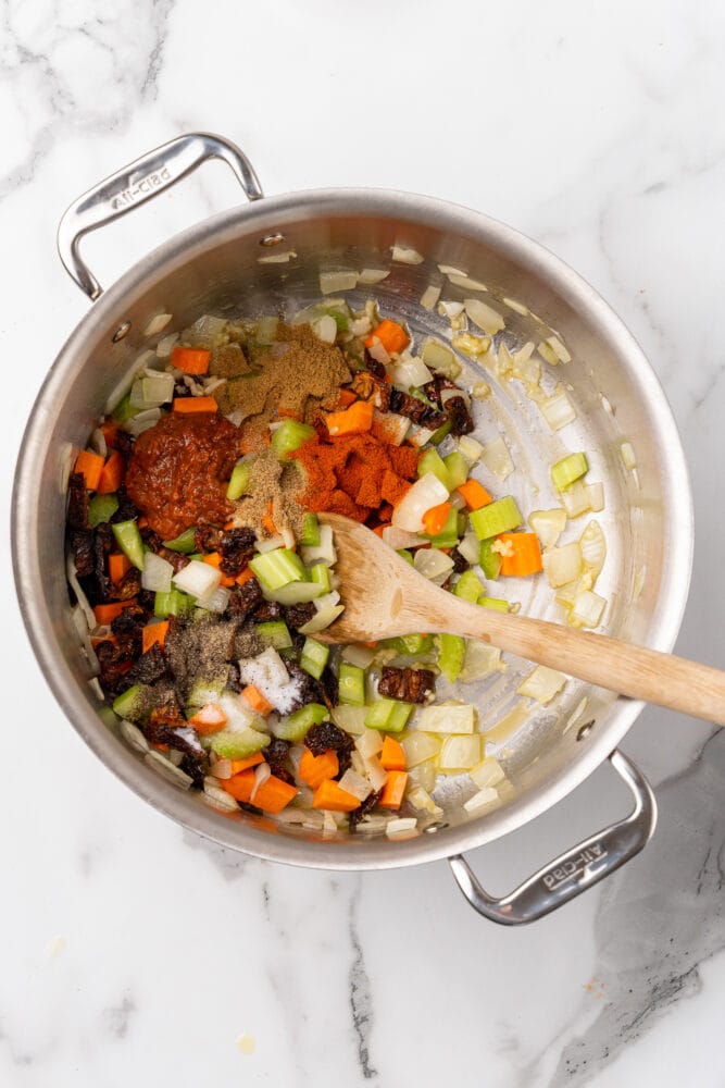 Sauteing vegetables with spices in a stainless steel soup pot.