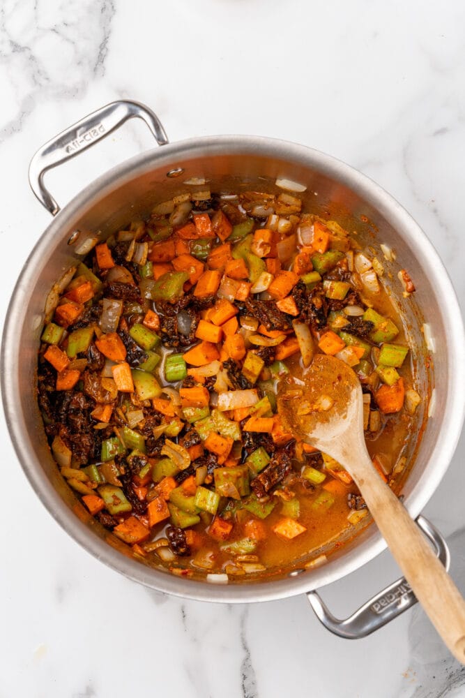 Adding some broth to soup pot with vegetables.