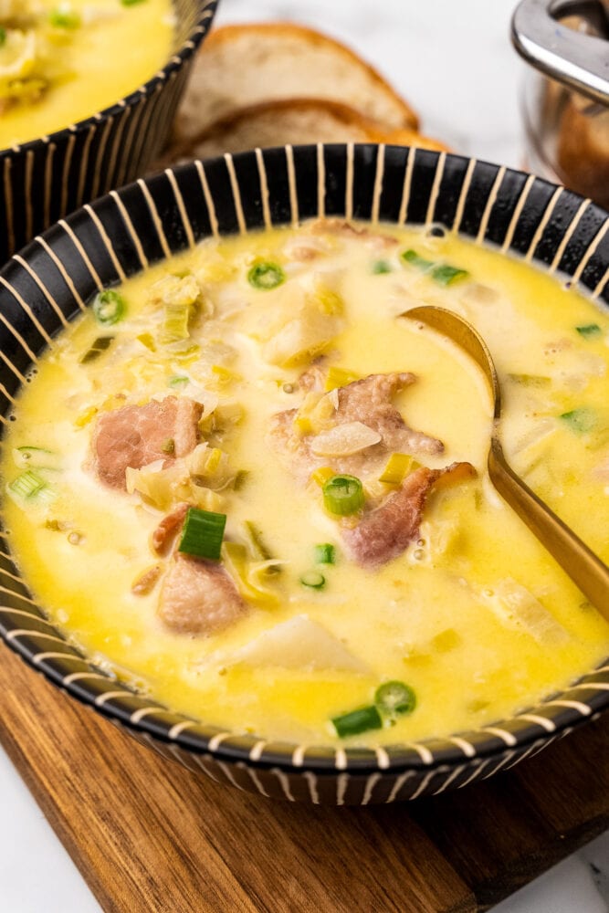 Comforting bowl of Irish colcannon soup. There are bits of bacon, onions, cabbage, and potatoes resting in a creamy buttery broth in a black striped bowl with a golden spoon.